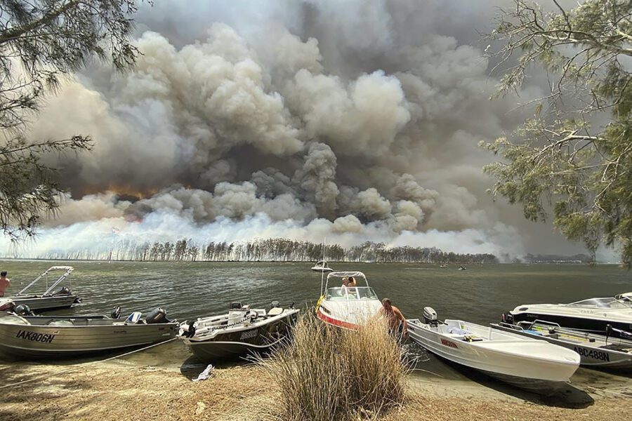 Boats are pulled ashore as smoke and wildfires rage behind Lake Conjola, Australia, Thursday, Jan. 2, 2020. Thousands of tourists fled Australia’s wildfire-ravaged eastern coast Thursday ahead of worsening conditions as the military started to evacuate people trapped on the shore further south. (Robert Oerlemans via AP)
