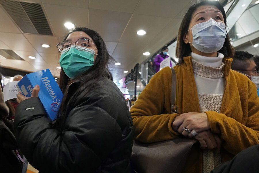 A woman holds a box of face mask as people queue up waiting to purchase face masks outside a shop in Hong Kong, Wednesday, Jan. 29, 2020. A viral outbreak that began in China has infected more than 6,000 people in the mainland and more than a dozen other countries. (AP Photo/Vincent Yu)