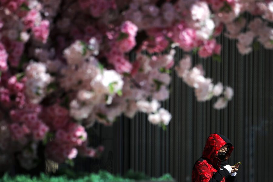 A masked woman browses her smartphone as she walks by the Wangfujing shopping district in Beijing, Tuesday, March 10, 2020. For most people, the new coronavirus causes only mild or moderate symptoms, such as fever and cough. For some, especially older adults and people with existing health problems, it can cause more severe illness, including pneumonia. (AP Photo/Andy Wong)
