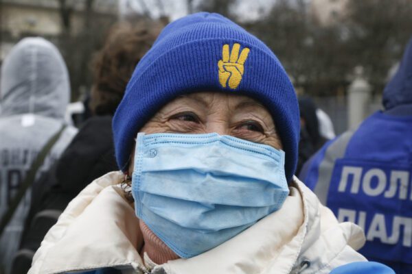An elderly woman in a face mask smiles as she attends a rally in front of the parliament building in Kyiv, Ukraine, Tuesday, March 17, 2020. Protesters demanded lawmakers to stop working amid nation-wide quarantine in order to prevent hastily adopting unpopular laws. In an additional set of measures preventing the spread of the new coronarivus, Ukrainian authorities ruled to close public places except food markets, pharmacies and gas stations starting from Tuesday in Kyiv and other regions, and restrict the use of public transport from Kyiv to other Ukrainian cities.  For most people, the new coronavirus causes only mild or moderate symptoms. For some it can cause more severe illness, especially in older adults and people with existing health problems. (AP Photo/Efrem Lukatsky)