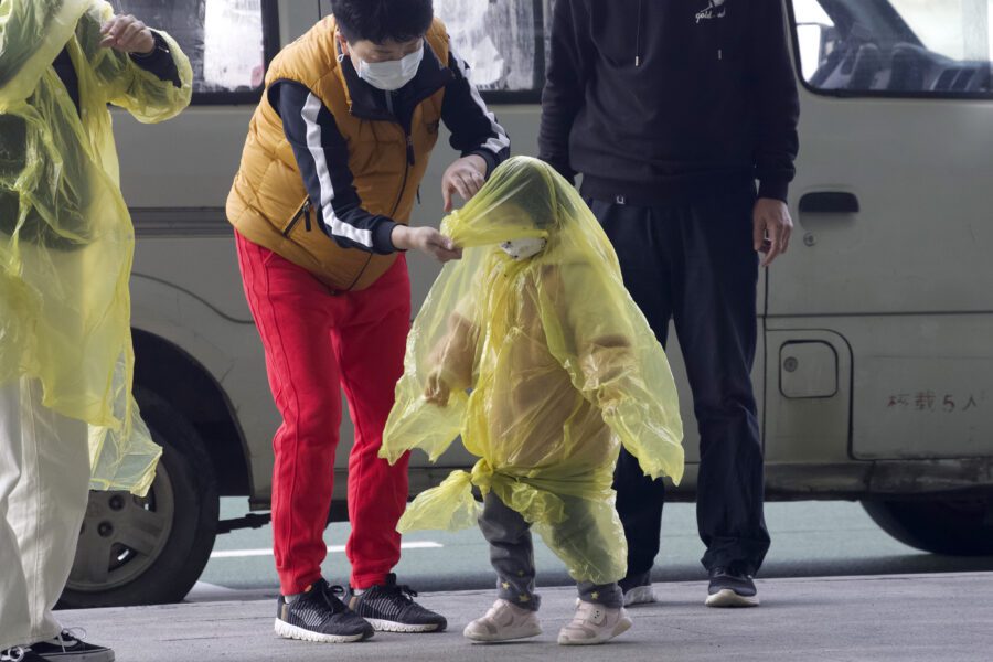 A woman wearing a face mask to protect against the spread of coronavirus puts a poncho on a child at Wuhan Tianhe International Airport in Wuhan in central China’s Hubei Province, Wednesday, April 8, 2020. Within hours of China lifting an 11-week lockdown on the central city of Wuhan early Wednesday, tens of thousands people had left the city by train and plane alone, according to local media reports. (AP Photo/Ng Han Guan)