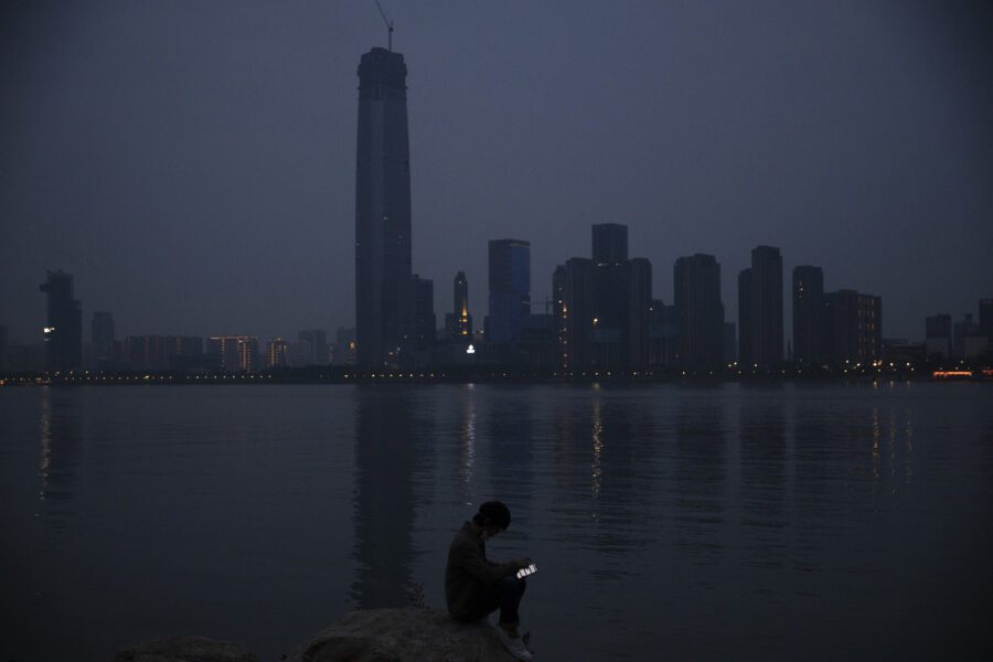 FILE – In this April 5, 2020, file photo, a man checks his mobile phone along the Yangtze River in Wuhan in central China’s Hubei province. As governments around the world consider how to monitor new coronavirus outbreaks while reopening their societies, many are starting to bet on smartphone apps to help stanch the pandemic. (AP Photo/Ng Han Guan, File)