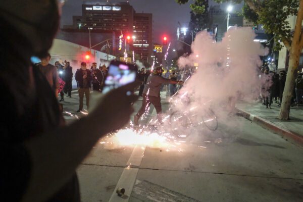 In this May 29, 2020, photo, protesters run through smoke as police officers start firing rubber bullets during a protest over the Minneapolis death of George Floyd in Los Angeles. Floyd died in police custody Monday in Minneapolis. (AP Photo/Ringo H.W. Chiu)