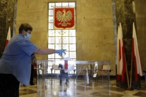 A resident, wearing face mask and protective gloves, casts a vote during presidential election in Warsaw, Poland, Sunday, June 28, 2020. The election will test the popularity of incumbent President Andrzej Duda who is seeking a second term and of the conservative ruling party that backs him. (AP Photo/Petr David Josek)