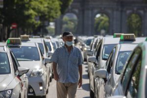 TRacxicoronavirus walks amid a taxi drivers protest in downtown Madrid, Spain, Tuesday, June 30, 2020. Taxi drivers are demanding  assistance due to lack of clients and private hire. (AP Photo/Manu Fernandez)
