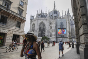 Pedestrians pass by a screen on the Duomo cathedral, showing a Moschino model during the Milan Digital Fashion Week, in Milan, Italy, Tuesday, July 14, 2020. Forty fashion houses are presenting previews of menswear looks for next spring and summer and pre-collections for women in digital formats, due to concerns generated by the COVID-19. (AP Photo/Luca Bruno) Pedestrians pass by a screen on the Duomo cathedral, showing a Moschino model during the Milan Digital Fashion Week, in Milan, Italy, Tuesday, July 14, 2020. Forty fashion houses are presenting previews of menswear looks for next spring and summer and pre-collections for women in digital formats, due to concerns generated by the COVID-19. (AP Photo/Luca Bruno)