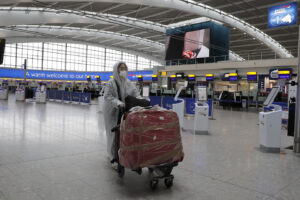 A traveller in protective clothing carries her luggage at Heathrow Airport in London, Wednesday, March 18, 2020. Britain’s Foreign Secretary Dominic Raab has taken the decision to advise British nationals against non-essential travel globally for an initial period of 30 days, and of course subject to ongoing review. For most people, the new coronavirus causes only mild or moderate symptoms, such as fever and cough. For some, especially older adults and people with existing health problems, it can cause more severe illness, including pneumonia.(AP Photo/Frank Augstein)