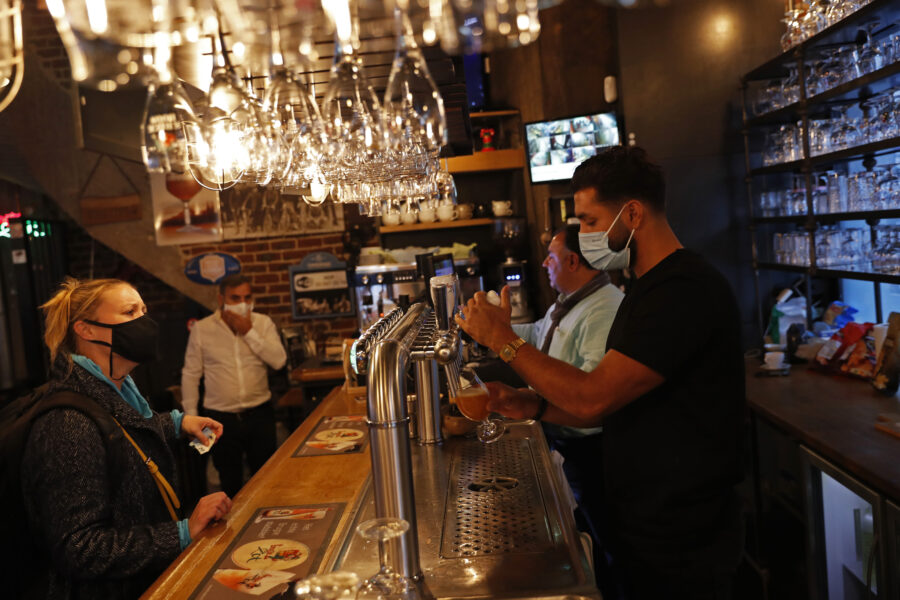 A bartender, wearing a face mask to fight against the spread of the coronavirus, serves a beer to a customer in a pub in Brussels, Wednesday, Oct. 7, 2020. Since bars in Brussels were forced to close as of Thursday for at least a month to deal with a massive surge in coronavirus cases while restaurants were allowed to remain open, the big question on the streets is: when is a bar a bar and when is a bar a restaurant. (AP Photo/Francisco Seco)