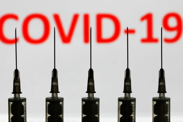 Medical syringes are seen with ‘covid-19’ sign displayed on a screen in the background in this illustration photo taken in Poland on October 12, 2020. (Photo illustration by Jakub Porzycki/NurPhoto via Getty Images)