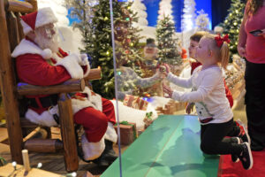 Julianna, 3, and Dylan, 5, Lasczak visit with Santa through a transparent barrier at a Bass Pro Shop in Bridgeport, Conn., Tuesday, Nov. 10, 2020.  Malls are doing all they can to keep the jolly old man safe from the coronavirus, including banning kids from sitting on his knee, completely changing what a Santa visit looks like.   (AP Photo/Seth Wenig)