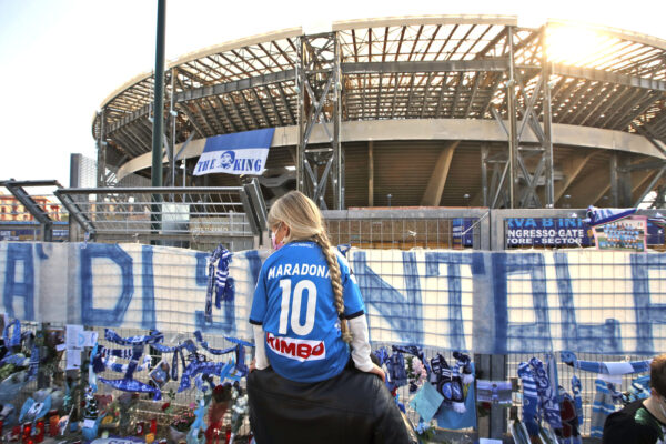 A girl sits on a man’s shoulders as she looks at gadgets and memorabilia commemorating soccer legend Diego Maradona outside the San Paolo stadium, in Naples, southern Italy, Thursday, Nov. 26, 2020. Maradona died Wednesday, Nov. 25, 2020 in Buenos Aires. (AP Photo/Alessandra Tarantino)