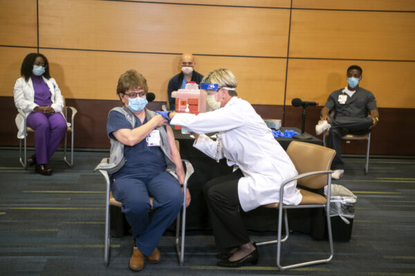 Charmaine Pykosh, an acute care nurse practitioner, receives Pfizer’s COVID-19 vaccine from Tami Minnier, chief quality officer, at UPMC Children’s Hospital of Pittsburgh, Monday, Dec. 14, 2020, in Lawrenceville. Ms. Pykosh was the first person out of five healthcare workers to receive the vaccine shortly after it arrived at the facility.  (Alexandra Wimley/Pittsburgh Post-Gazette via AP)