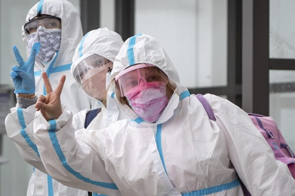 People wearing protective face masks, goggles and Tyvek suits, who said they traveled from Colombia gesture while waiting for a car rental company shuttle, after arriving at Vancouver International Airport in Richmond, British Columbia., Thursday, Dec. 31, 2020. Beginning January 7, air travelers arriving in Canada will be required to provide proof of a negative COVID-19 test conducted within 72 hours of boarding the plane. (Darryl Dyck/The Canadian Press via AP)