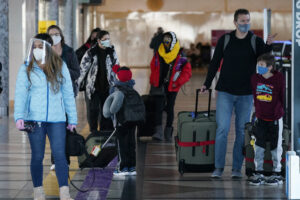 Travelers wear face masks while checking in at the ticket counter of Frontier Airlines in the main terminal of Denver International Airport late Thursday, Dec. 31, 2020, in Denver. (AP Photo/David Zalubowski)