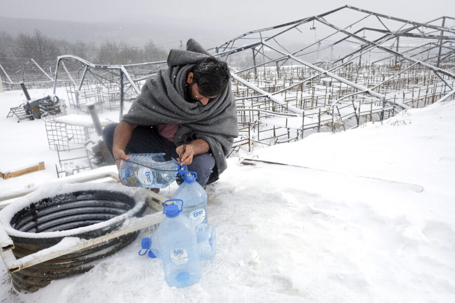 A migrant uses plastic bottles to take water out of a well during a snowfall at the Lipa camp, outside Bihac, Bosnia, Monday, Jan. 11, 2021. Aid workers say migrants staying at a camp in northwestern Bosnia have complained or respiratory and skin diseases after spending days in make-shift tents and containers amid freezing weather and snow blizzards. Most of the hundreds of migrants at the Lipa facility near Bosnia’s border with Croatia on Monday have been accommodated in heated military tents following days of uncertainty after a fire gutted most of the camp on Dec. 23. (AP Photo/Kemal Softic)