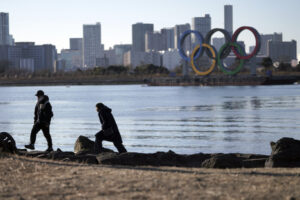 A man and a woman walk near the Olympic rings floating in the water in the Odaiba section in Tokyo Wednesday, Jan. 20, 2021. The postponed Tokyo Olympics are to open in just six months. Local organizers and the International Olympic Committee say they will go ahead on July 23. But it’s still unclear how this will happen with virus cases surging in Tokyo and elsewhere around the globe. (AP Photo/Eugene Hoshiko)