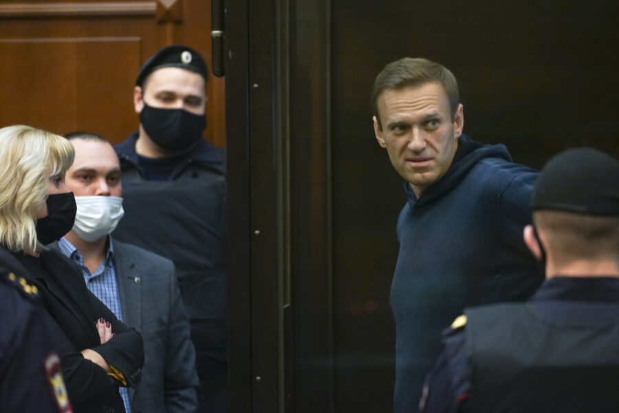 In this handout photo provided by Moscow City Court Russian opposition leader Alexei Navalny talks to his lawyers standing in the cage during a hearing to a motion from the Russian prison service to convert the suspended sentence of Navalny from the 2014 criminal conviction into a real prison term in the Moscow City Court in Moscow, Russia, Tuesday, Feb. 2, 2021. (Moscow City Court via AP)