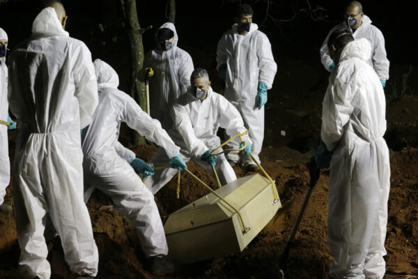 Cemetery workers lower the coffin of a COVID-19 victim into his grave at the Vila Formosa cemetery in Sao Paulo, Brazil, late Wednesday, March 31, 2021. Because of the increased number of deaths in the city, the burial service in some public cemeteries has been extended to the hours of the night. (AP Photo/Nelson Antoine)