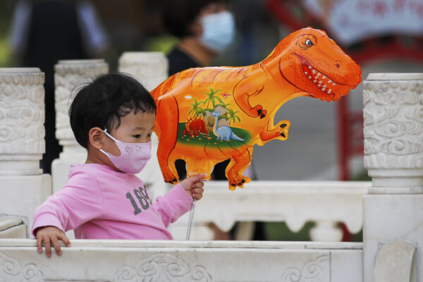 A child wearing a face mask to help curb the spread of the coronavirus holds a dinosaur shaped balloon walks at a public park in Beijing, Sunday, May 16, 2021. (AP Photo/Andy Wong)