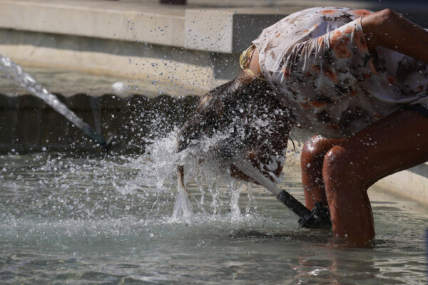 A woman cools-off in a fountain in downtown Milan, Italy, Tuesday, Aug. 10, 2021. Temperatures are expected to go over 45 degrees in some parts of Italy in the next days. (AP Photo/Antonio Calanni)
