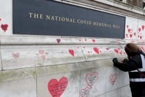 A plaque dedication as people paint red hearts onto the COVID-19 Memorial Wall mourning those who have died, along the embankment opposite the Houses of Parliament on the Embankment in London, Monday, April 5, 2021. Hearts are being painted onto the wall in memory of the many thousands of people who have died in the UK from coronavirus. (AP Photo/Frank Augstein)