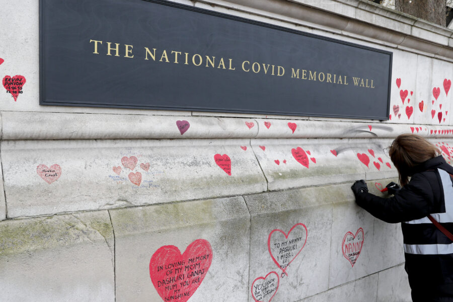 A plaque dedication as people paint red hearts onto the COVID-19 Memorial Wall mourning those who have died, along the embankment opposite the Houses of Parliament on the Embankment in London, Monday, April 5, 2021. Hearts are being painted onto the wall in memory of the many thousands of people who have died in the UK from coronavirus. (AP Photo/Frank Augstein)