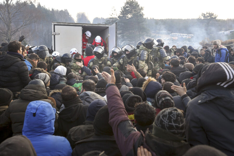 Belarusian servicemen control the situation while migrants get humanitarian aid as they gather at the Belarus-Poland border near Grodno, Belarus, Friday, Nov. 12, 2021. Thousands of people from Middle Eastern nations devastated by conflict have been trying to slip into the European Union. They are using a backdoor that was surreptitiously opened by Belarus a few months ago. (Ramil Nasibulin/BelTA pool photo via AP)