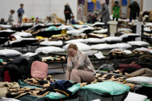 A woman puts her head in her hands as she sits on a cot in a shelter, set up for displaced persons fleeing Ukraine, inside a school gymnasium in Przemysl, Poland, Tuesday, March 8, 2022. U.N. officials said Tuesday that the Russian onslaught has forced more than 2 million people to flee Ukraine. (AP Photo/Markus Schreiber)