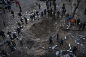 People gather around a crater created by a bomb that heavily damaged buildings and cars in Kyiv, Ukraine, Sunday, March 20, 2022.(AP Photo/Rodrigo Abd)