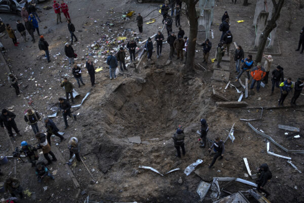 People gather around a crater created by a bomb that heavily damaged buildings and cars in Kyiv, Ukraine, Sunday, March 20, 2022.(AP Photo/Rodrigo Abd)