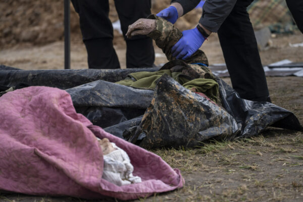 A policeman examines the corpse of a Ukrainian soldier removed from a mass grave in Bucha, in the outskirts of Kyiv, Ukraine, Monday, April 11, 2022. (AP Photo/Rodrigo Abd)