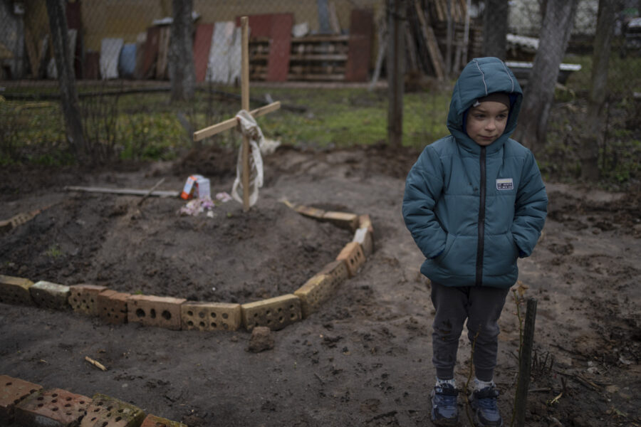 In the courtyard of their house, Vlad Tanyuk, 6, stands near the grave of his mother Ira Tanyuk, who died because of starvation and stress due to the war, on the outskirts of Kyiv, Ukraine, Monday, April 4, 2022. (AP Photo/Rodrigo Abd)