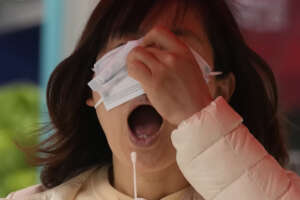 A woman opens her mouth for a swab during mass COVID tests on Friday, April 29, 2022, in Beijing. (AP Photo/Ng Han Guan)