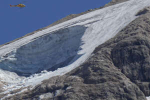 A rescue helicopter hovers over the Punta Rocca glacier near Canazei, in the Italian Alps in northern Italy, Monday, July 4, 2022, a day after a huge chunk of the glacier broke loose, sending an avalanche of ice, snow, and rocks onto hikers. Rescuers said conditions downslope from the glacier, which has been melting for decades, were still too unstable to immediately send rescuers and dogs into the area to look for others buried under tons of debris. (AP Photo/Luca Bruno)