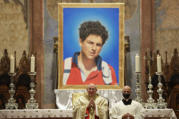 An image of 15-year-old Carlo Acutis, an Italian boy who died in 2006 of leukemia, is seen during his beatification ceremony celebrated by Cardinal Agostino Vallini, center, in the St. Francis Basilica, in Assisi, Italy, Saturday, Oct. 10, 2020. (AP Photo/Gregorio Borgia)