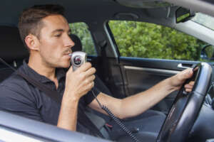 Man in car blowing into breathalyzer Man in car blowing into breathalyzer