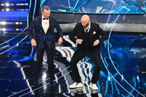 John Travolta, il balletto ‘scandaloso’ e il polverone sulle scarpe U-power ‘boom di vendite’: sospetto pubblicità occulta con l’ad Uzzeni sorridente e soddisfatto sotto al palco di Sanremo 2024