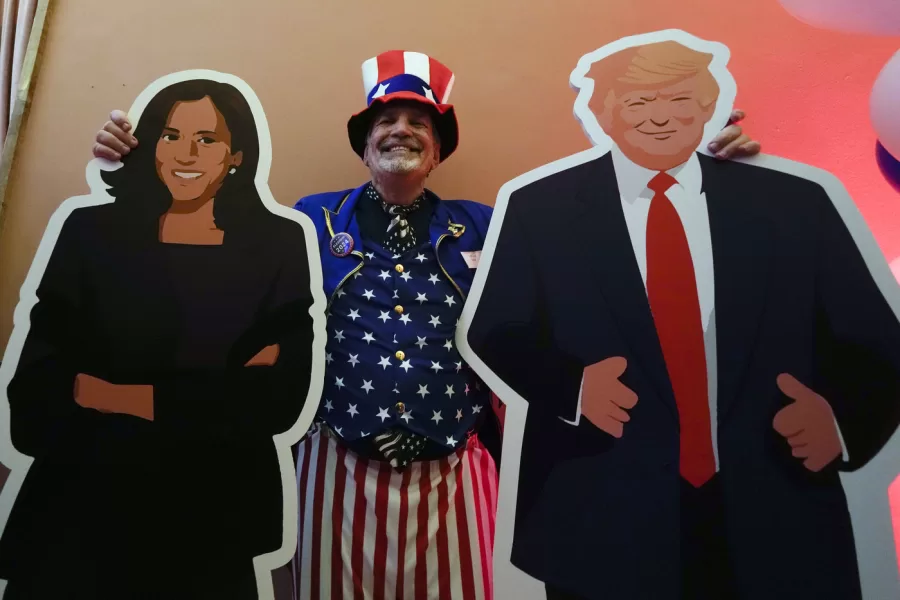 U.S. Consulate General Services Officer Timothy Lockwood poses with cardboards of Kamala Harris and Donald Trump during the Election Night event in Milan, Italy, Tuesday, Nov. 5, 2024. (AP Photo/Luca Bruno)
