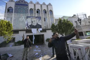 Syrian opposition fighters take selfie at the damaged entrance of the Iranian embassy in Damascus, Syria, Sunday, Dec. 8, 2024. (AP Photo/Hussein Malla)