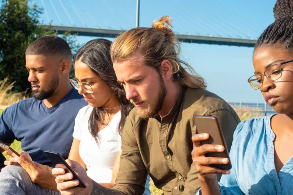 Focused multiracial friends using smartphones. Concentrated young male and female friends gathering together, sitting and using cell phones in park. Technology concept
