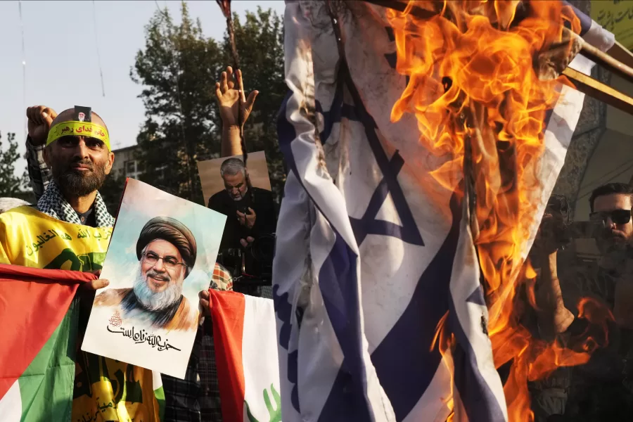 An Iranian demonstrator holds a poster of slain Hezbollah leader Hassan Nasrallah reading in Farsi: “Hezbollah is alive,” as a representation of the Israeli flag is set on fire in an anti-Israeli gathering at Felestin (Palestine) Sq. in Tehran, Iran, Tuesday, Oct. 8, 2024. (AP Photo/Vahid Salemi)
