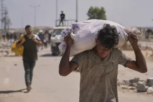 A Palestinian carries a bag containing aid near a Gaza Humanitarian Foundation distribution center operated by the U.S.-backed organization, in Netzarim, central Gaza Strip, Monday, Aug. 4, 2025. (AP Photo/Abdel Kareem Hana)