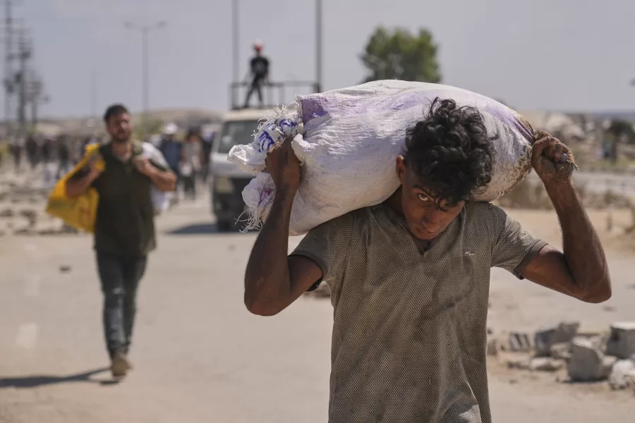 A Palestinian carries a bag containing aid near a Gaza Humanitarian Foundation distribution center operated by the U.S.-backed organization, in Netzarim, central Gaza Strip, Monday, Aug. 4, 2025. (AP Photo/Abdel Kareem Hana)