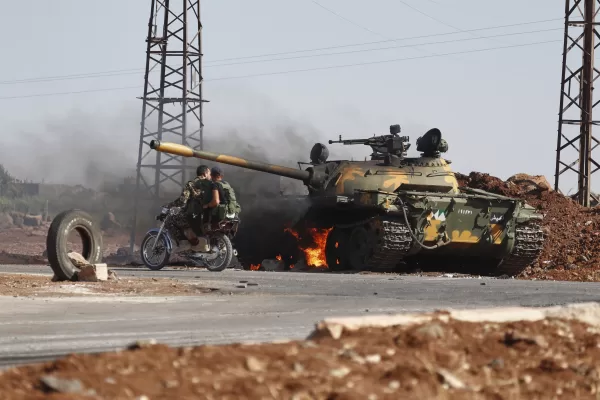 Syrian government soldiers on a motorcycle pass by a burning tank on the outskirts of Sweida city, where clashes erupted between Druze militias and Sunni Bedouin clans, in southern Syria, Monday, July 14, 2025. (AP Photo/Omar Sanadiki)