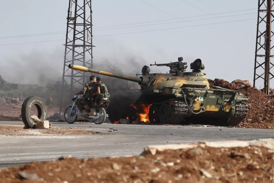 Syrian government soldiers on a motorcycle pass by a burning tank on the outskirts of Sweida city, where clashes erupted between Druze militias and Sunni Bedouin clans, in southern Syria, Monday, July 14, 2025. (AP Photo/Omar Sanadiki)