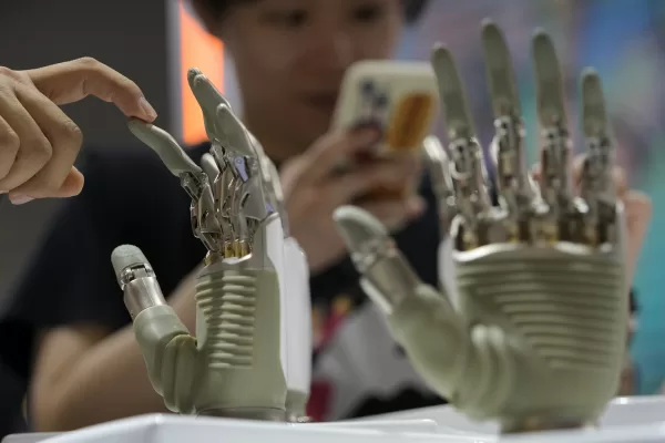 A visitor touches a humanoid robot hand on display at an AI exhibition booth during the 2024 The World Artificial Intelligence Conference (WAIC) & High-Level Meeting on Global AI Governance with the themed “Governing AI for Good and for All” at the Shanghai Expo Center Multifunction Hall in Shanghai China, Thursday, July 4, 2024. (AP Photo/Andy Wong)