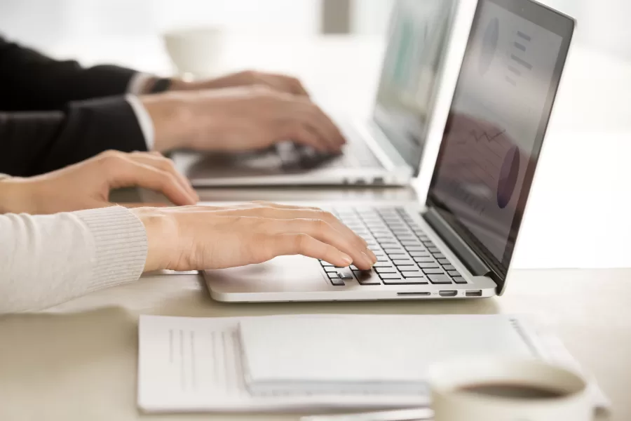 Close up image of female and male employers hands typing together on laptop keyboards at desk. Financial experts monitoring economical indicator online. E-commerce business team daily computer routine