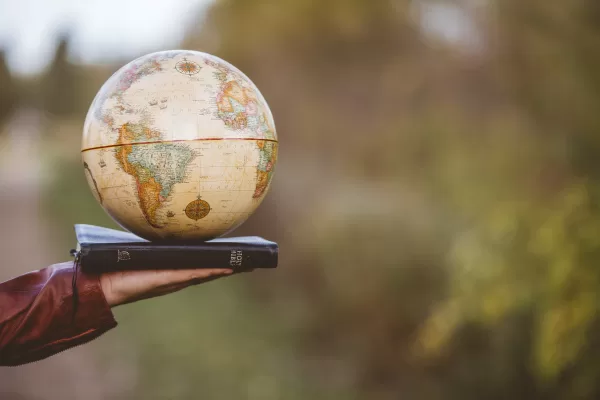 A closeup shot of a person holding bible with desk globe on top with a blurred background A closeup shot of a person holding bible with desk globe on top with a blurred background