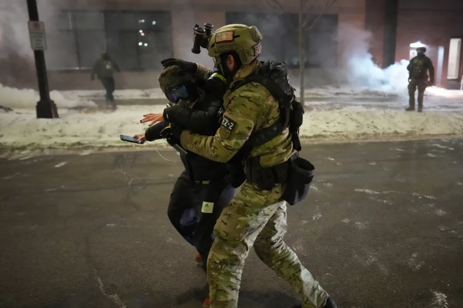 A federal agent holds a person as the agents try to clear the demonstrators near a hotel, using tear gas during a noise demonstration protest in response to federal immigration enforcement operations in the city Sunday, Jan. 25, 2026, in Minneapolis. (AP Photo/Adam Gray)