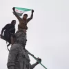 Syrian government soldiers wave a Syrian flag after climbing atop a statue of a female Kurdish fighter, following the takeover of the town from U.S.-backed Syrian Democratic Forces (SDF) during an ongoing push against Kurdish-led forces, in Tabqa, eastern Syria, Sunday, Jan. 18, 2026. (AP Photo/Omar Albam)